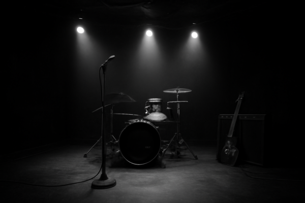 Panggung klub rock kecil dengan mikrofon, drum, dan gitar bersandar, suasana sunyi sebelum pertunjukan
